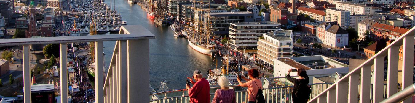 Vier Menschen stehen auf der Aussichtsplattform SAIL City in Bremerhaven und blicken auf das Hafenbecken voller Schiffe.