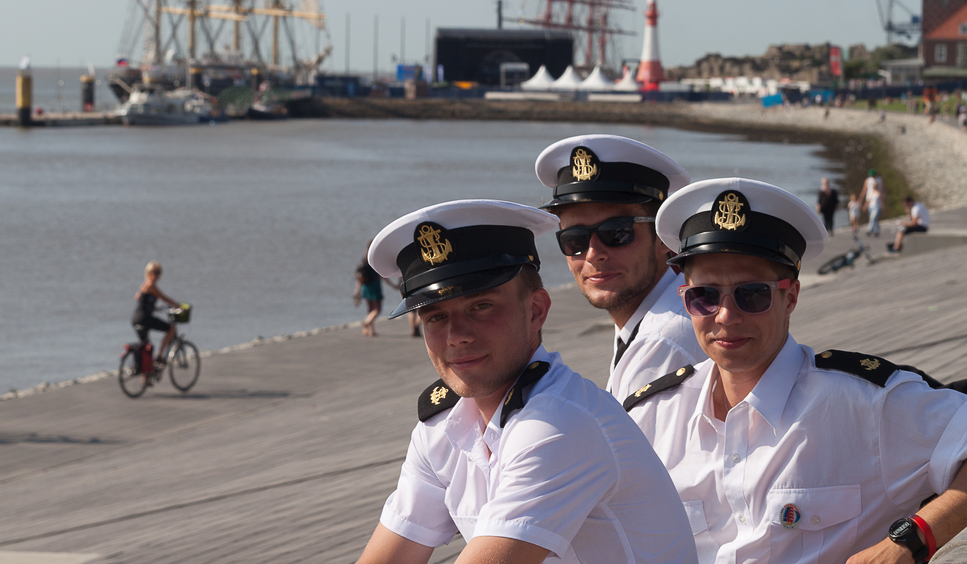 Three sailors sit at the dike and smile into the camera.
