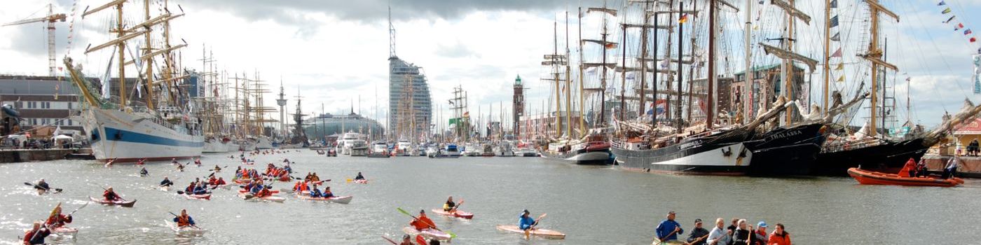 Many people paddle in kayaks and canoes in a harbor basin.
