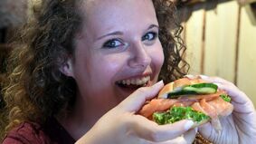 A young woman is eating a fish sandwich.