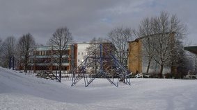 Im Hintergrund ist die Paula-Modersohn-Schule und einige kahle Bäume abgebildet. Im Vordergrund sieht man ein großes Klettergerüst. Auf dem Boden liegt Schnee.