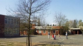 Im Vordergrund steht ein kahler Baum, dahinter spielen mehrere Kinder. Im Hintergrund sieht man die Fritz-Husmann-Schule - Dependance / St.-Ansgar-Schule.