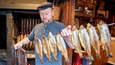 Man holding long stick with smoked fish in hand