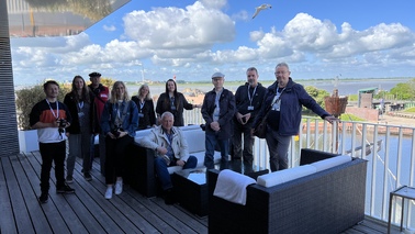 A group of people is standing and sitting on the terrace of the NEW YORK BAR of "The Liberty Hotel Bremerhaven".