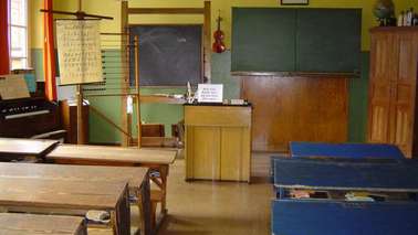 A decorated classroom with blackboard, benches and teacher's desk.