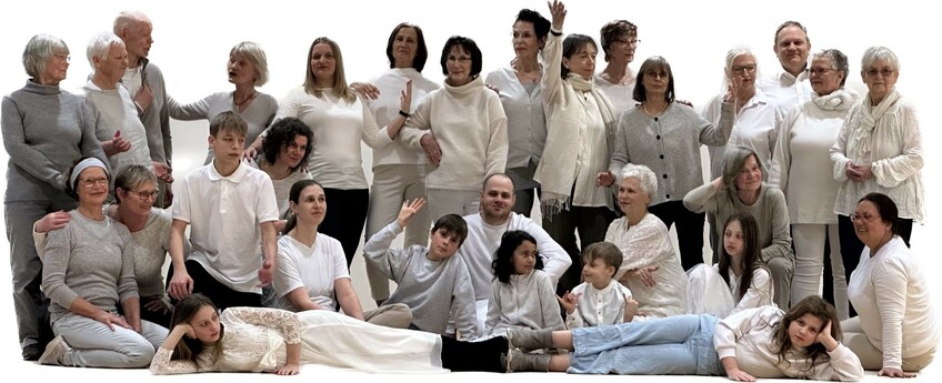 Menschen unterschiedlicher Generationen posieren für eine Gruppenaufnahme. Alle tragen helle Kleidung, wodurch ein sehr einheitliches Bild entsteht.