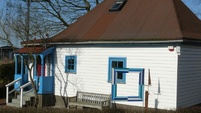 Das Wilkeatelier am Hafen. Ein weißes Holzhäuschen mit blauen Fensterrahmen.