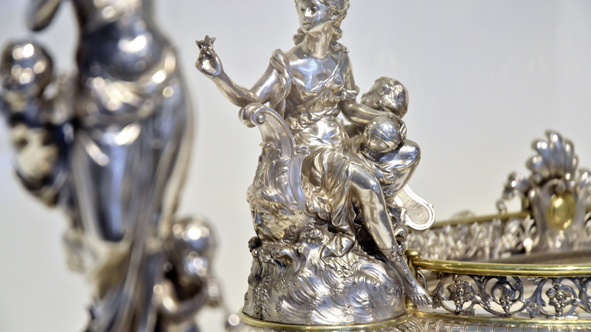 Das Foto zeigt ein Detail des silbernenTafelaufsatzes, der anlässlich der Silberhochzeit von Peter und Sophie Rickmers 1887 bei Wilkens & Söhne in Bremen gefertigt wurde. Die sitzende Frauenfigur stellt eine Allegorie auf die Schifffahrt dar.