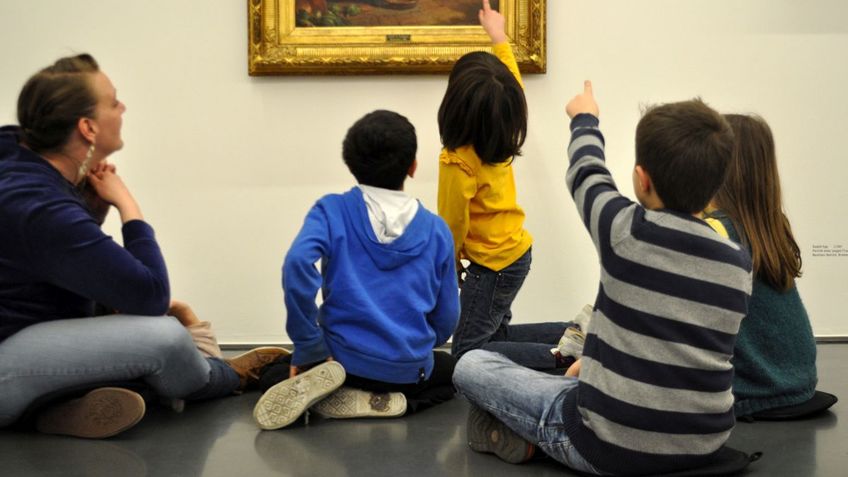 Kinder sitzen vor einem Gemälde.
