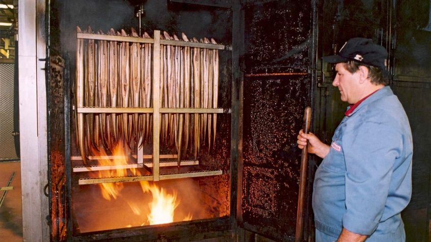  A man stands in front of a smokehouse.