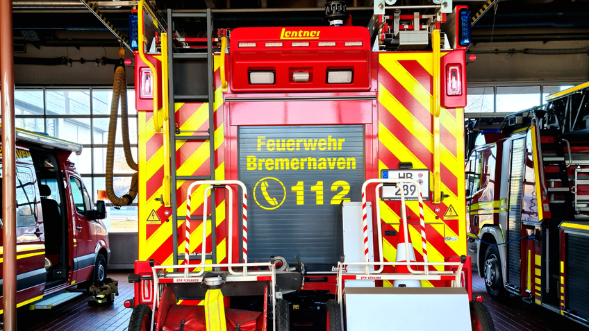 Die Fahrzeughalle der Feuerwehr Bremerhaven. Es sind der Einsatzleitwagen, das Löschfahrzeug und die Drehleiter von hinter zu sehen.