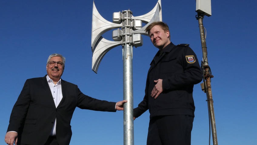 Oberbürgermeister Melf Grantz und Sören Makel von der Feuerwehr Bremerhaven stehen neben der ersten modernen Warnsirene, die in Bremerhaven errichtet wurde 