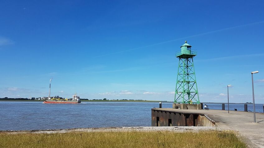 Ein grüner Leuchtturm am Wasser.