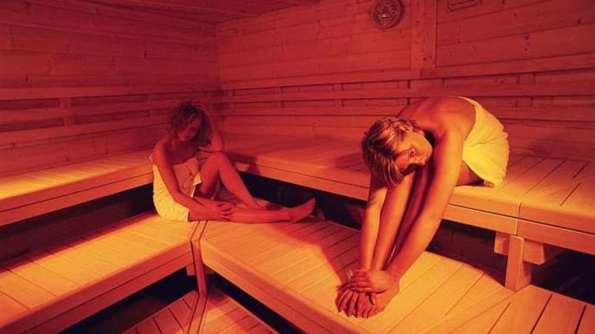  Two women lie on wooden benches in a saunas area.