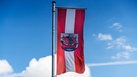 Rot-weiße Flagge Bremerhavens mit dem Stadtwappen einer Kogge vor blauem Himmel