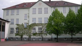 Zu sehen ist die Rückseite der Allmersschule vom Schulhof aus fotografiert. Rechts im Bild sind Bäume zu sehen.