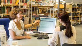 An employee is advising a customer in a library.