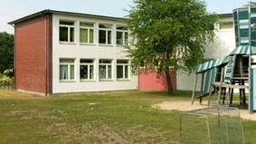 Im Vordergrund steht ein großes Spielgerüst und zwei kleine Fußballtore aus Metall.  Im Hintergrund ist ein Baum und die Friedrich-Ebert-Schule zu sehen.