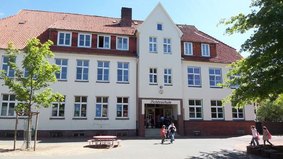 Der Eingang der Fichteschule wurde vom Pausenhof aus fotografiert. Links und Rechts sind Bäume zu sehen.