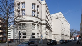 Zu sehen ist das Lloyd Gymnasium (Haus Grazer Straße) in der Frontansicht. In der Mitte des Bildes sieht man einen großen Baum. 