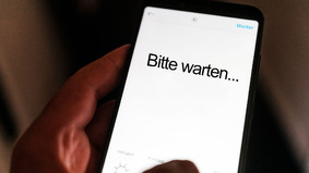Smartphone mit "Bitte warten"-Text