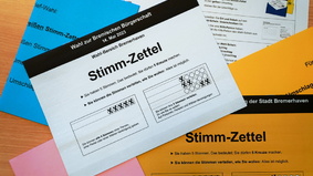 Stimmzettel in verschiedenen Farben durcheinander auf einem Tisch ausgebreitet.