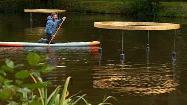Ein Mann kniet auf einem SUP-Board und paddelt zu großen Lichtobjekten über das Wasser