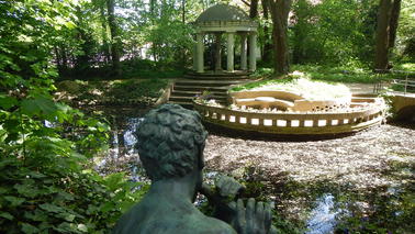 A stone-built pavilion in front of a pond.