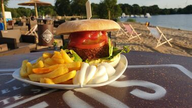 A served hamburger with french fries with a view on the lake.