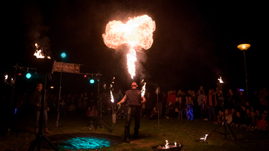 Ein Mann steht im Zentrum einer Besuchermenge und spuckt einen Feuerball. 