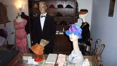 Verschiedene Hüte und ein Verkäufer in einem Ausstellungsraum.
