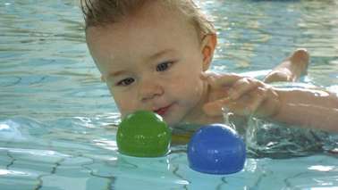 Ein Baby liegt im Wasser und spielt mit Bällen.