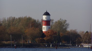 A lighthouse, striped red and white, located between trees.