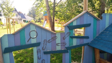 Spielhaus mit gedruckten Fußspuren und Lupe auf Holzlatten