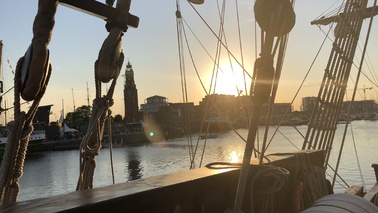 Blick von Segelschiff zwischen den Seilen durch auf den Hafen bei Sonnenuntergang.