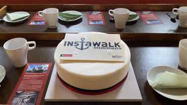 Eine gedeckte Tafel mit einer Torte. Auf der Torte steht "InstaWalk Bremerhaven".