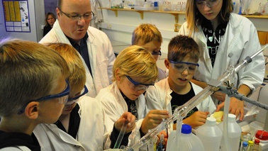 Besucher in weißen Kitteln und Schutzbrillen in einem Chemielabor