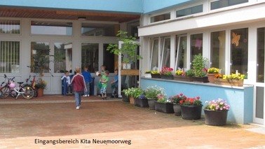 Eingangsbereich der Kindertagesstätte, blaues Gebäude mit Blumen