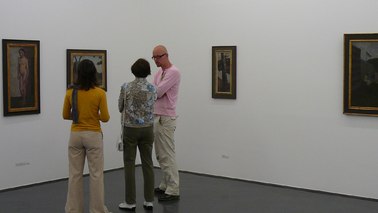 Drei Personen stehen in einem Raum und schauen sich Bilder an.