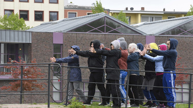 Eine Gruppe Personen mit Kapuzen drängen sich in einer Performance in Gitter.