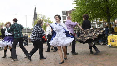 Menschen tanzen draußen Square Dance. Einige tragen große Petticoatröcke.