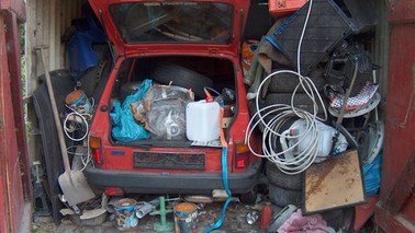 Auto in einer offenen Garage, sowohl das Fahrzeug als auch die Garage sind völlig vermüllt
