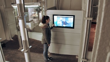 Eine junge Frau steht vor einem Informationsbildschirm.