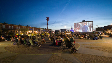 Menschen sitzen vor großer Filmleinwand im Freien