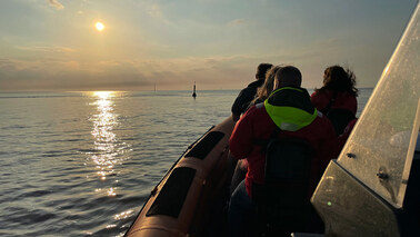 Three people sailing on RIB boat towards sunset