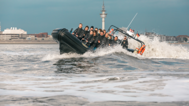 Zu sehen ist ein Schnell-Schlauchboot mit Menschen auf dem Wasser sowie viele Wellen.