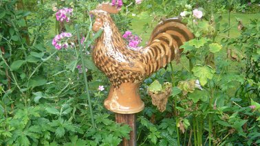 Ein Hahn als Skulptur in einem Garten.
