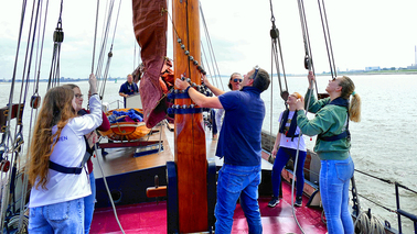 Menschen hissen ein Segel an Bord eines Schiffes.