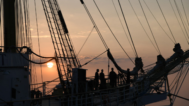Segelschiff bei Sonnenuntergang mit Mensch an Bord.
