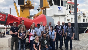 A group of people is standing in front of a ship for a group picture.
